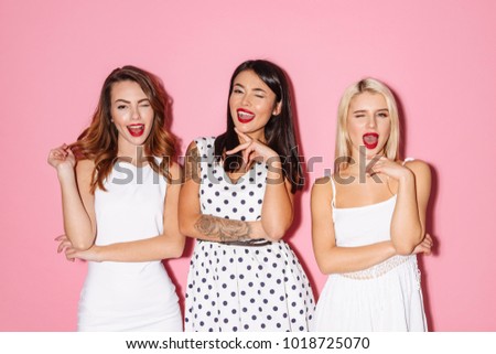 Picture of three young cute girls friends standing isolated over pink background looking camera winking.