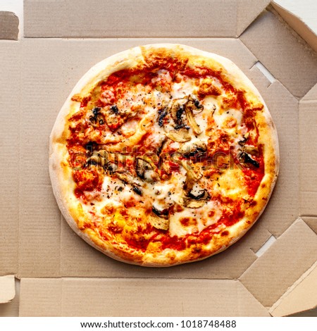 Pizza in a cardboard box on bright  background  with pepperoni, cherry tomatoes, cheese and tomato sauce. Pizza delivery, menu.