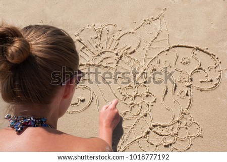 Young girl draws on the sand on the beach a zentangle, doodle