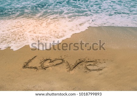 "Love" written on a sandy beach as the ocean water approaches.