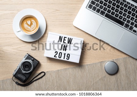 New in 2019 writing in lightbox with camera, coffee mug and laptop lying on photographer office desk as flat lay