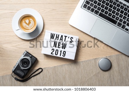 What's new 2019 writing in lightbox with camera, coffee mug and laptop lying on photographer office desk as flat lay