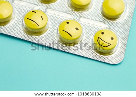 Yellow pills andfunny faces in a blister on a blue background. The concept of antidepressants and healing