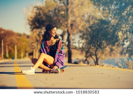happy woman sits on a skateboard against a background of trees and mountains