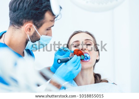 Young woman during innovative oral treatment with cordless LED curing light machine for whitening and restoration in the dental office of an experienced dentist Royalty-Free Stock Photo #1018855015