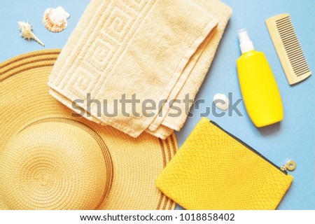 Women's sun hat, beige towel, yellow cosmetic bag, sunscreen bottle and seashells. Summer holiday, beach relaxation. Flat lay composition. Top view photo with many items