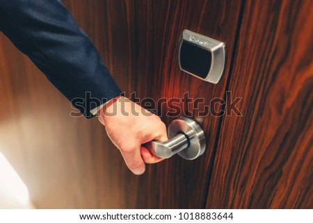 Man in a suit opens the door to the hotel room. The hotel door young man holding the handle in front of an electronic sensor door. Stylishly toned photo