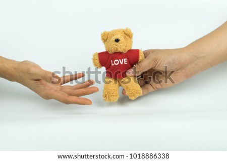 Hand giving a little teddy bear to another hand on white background.