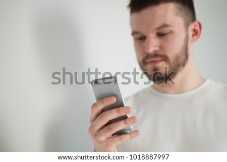 The phone in the hand of caucasian handsome beard man in a white t-shirt