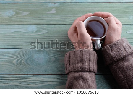 A young man warms his hands about a cup of hot tea