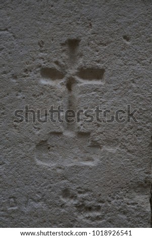 close up view of a small cross dug in the stone. Religious symbol representing jesus christ crucifixion. Minimalist picture with just one sculpted element. Beige colored and textured surface.