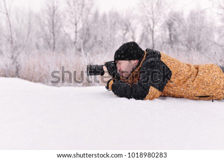 The young man, a photographer takes pictures on the camera in the winter sunny day on a blurred background at the forest,
