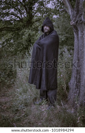 Hooded man wearing a cloak in a mysterious fantasy forest setting.