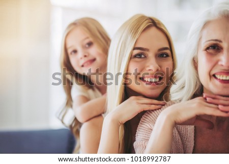 Little cute girl, her attractive young mother and charming grandmother are spending time together at home. Women's generation. Happy International Women's Day!