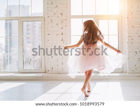 Cute little girl in beautiful dress is dancing at light sunny room Royalty-Free Stock Photo #1018993579