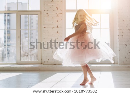 Cute little girl in beautiful dress is dancing at light sunny room Royalty-Free Stock Photo #1018993582
