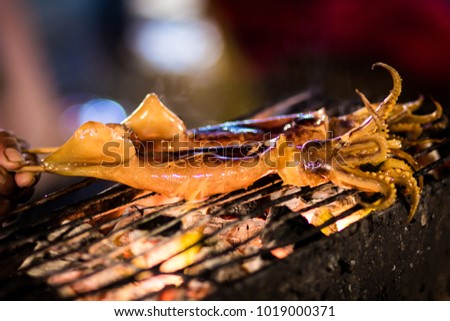 De focused Grilled squid in Thailand night market. Blurred picture. Grain photo. Noise Background. Blurred Background.