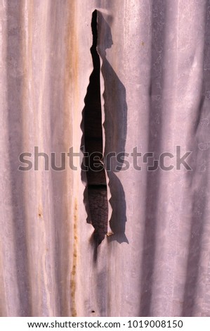 Close up of an old, gray corrugated steel wall with a large jagged tear running vertically along the metal