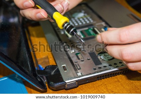 Disassembly of the netbook, elimination of breakdowns, repair of equipment. Hands with a screwdriver, the inside of the laptop. The foreground is blurred. Royalty-Free Stock Photo #1019009740