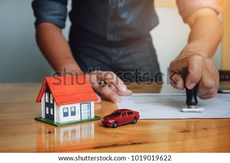 Business man pressing rubber stamp on insurance house&car document. Agreement and contract concept.