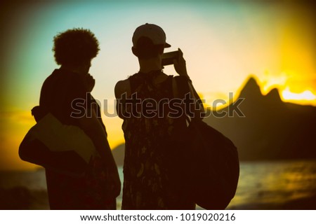 Scenic silhouettes of two unidentifiable tourists taking a photo of Two Brothers Mountain from sunset viewpoint at Arpoador, in Ipanema Beach, Rio de Janeiro, Brazil