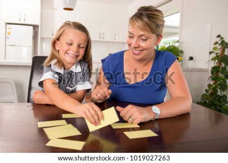 lovely sweet and happy 6 years old daughter learning reading with flash card words game at home kitchen playing with her young beautiful mother in lifestyle and education concept