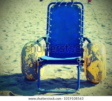 wheelchair with large inflatable wheels on the beach with vintage style effect