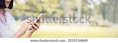 Closeup woman in white shirt smile read message to mobile phone, against green of summer park. Technology and communication concept banner (blur)