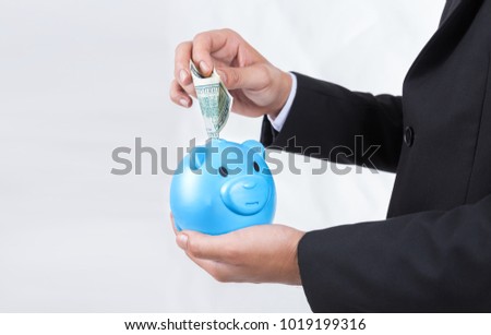 Male hand putting bank dollar into a piggy bank.