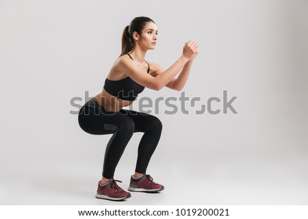 Image of sporty athletic woman in sneakers and tracksuit squatting doing sit-ups in gym isolated over gray background Royalty-Free Stock Photo #1019200021