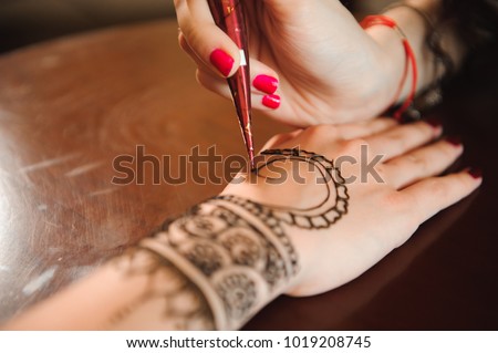 Master mehndi draws henna on a female hand.