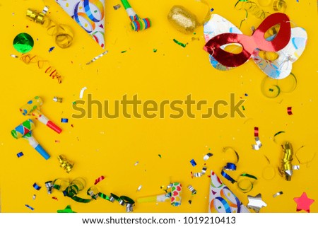 Bright colorful carnival or party scene of confetti and masks on yellow background. Flat lay style, birthday or party greeting card with copy space.