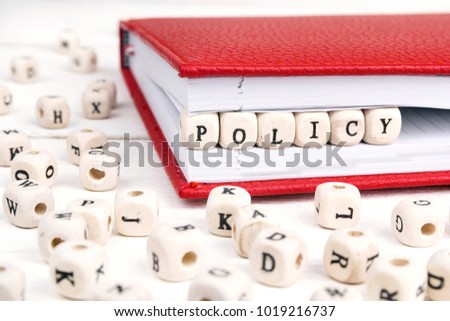 Word Policy written in wooden blocks in red notebook on white wooden table. Wooden abc.