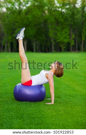 Young slim woman making exercises on fitball, outdoor