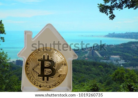 Bitcoin coin in a metal house on a sea cost background. Rent or buy a house for bitcoins.