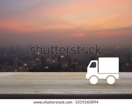 Truck delivery icon on wooden table over blur of cityscape on warm light sundown, Transportation business concept