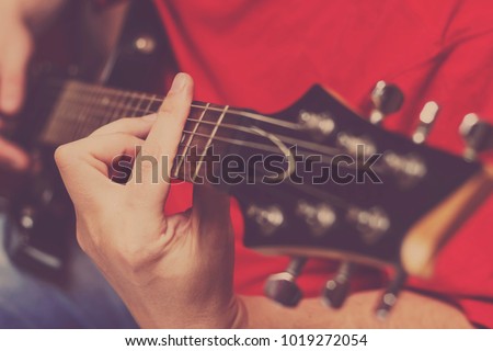 Closeup of hands of a  guy playing electrical guitar on a red background ,with only his fingers in focus