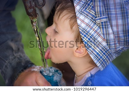 Child in profile drinking water from a stream of water in nature in the summer