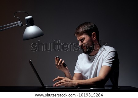 man sitting at desk with laptop in hand phone on black background                               