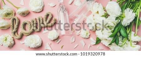 Saint Valentines Day layout. Flat-lay of white ranunculus flowers, champaign glasses and word love over light pink background, top view. Greeting card or wedding invitation