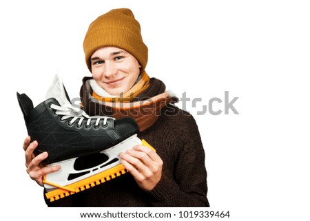 White young guy in a hat and sweater and scarf, holds skates in his hands, isolated on a white background.