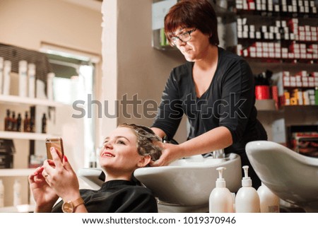 Hairdresser and a woman in a beauty salon during a hair wash. Woman with a mobile phone.