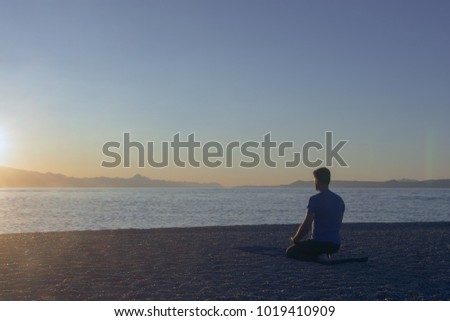 Adult man meditating on beach in the morning at sunrise