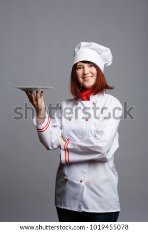 Photo of brunette chef in white robe and cap with empty plate in hand