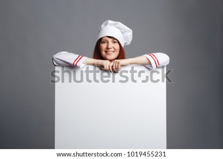 Photo of smiling brunette chef in white dressing-gown cap with empty paper in hands