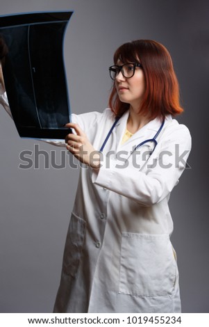 Image of female doctor in glasses and white robe with looking at x-ray on empty gray background
