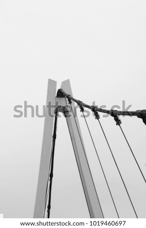 A black and white photo of a suspension bridge. The perspective is from the bottom of the bridge and looking up.