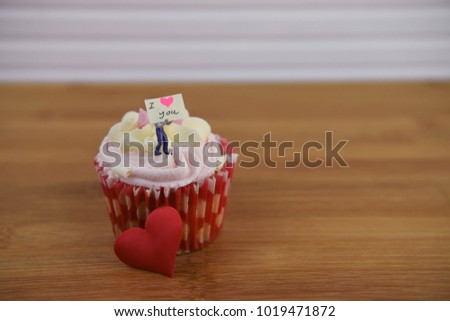 a strawberry and cream flavor cupcake for valentines day decorated with a miniature person figurine holding a sign and red love hearts 