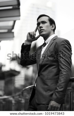 Black and white photo of Business man with suit standing in front of the modern office. Attractive young businessman using a cell phone. Standing in front of a modern office building.