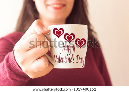 woman with beautiful smile drinking a coffee and  happy valentine's day text painted on cup 